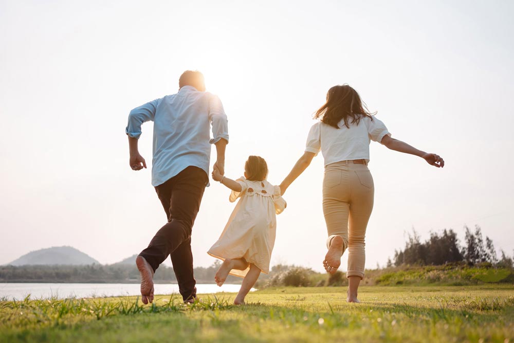 Mamma, pappa och barn som håller hand och springer över en äng