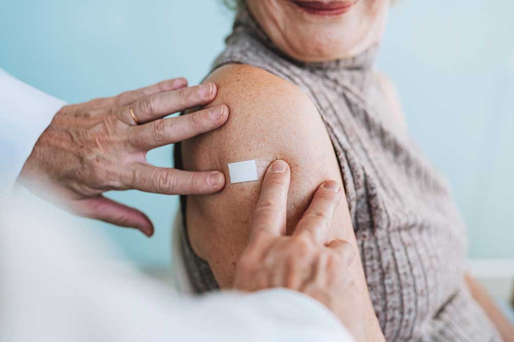 Sjukvårdspersonal sätter ett plåster på en äldre kvinnas överarm efter vaccination