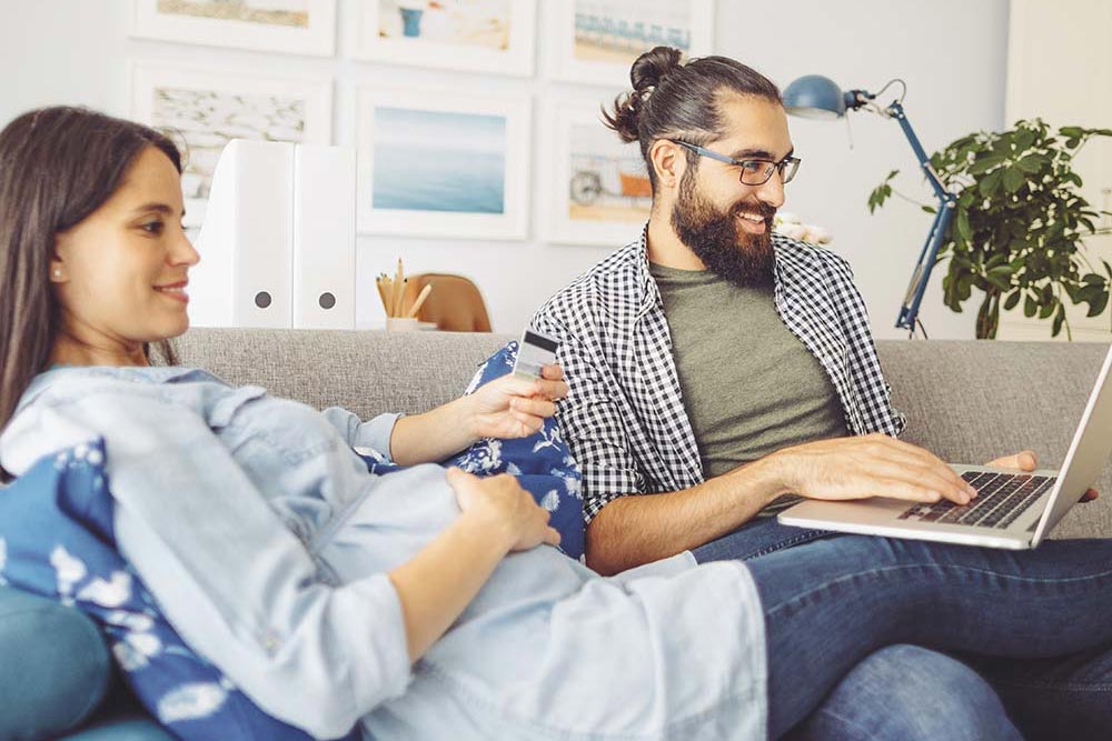 En gravid kvinna som sitter med sin man i soffan framför en laptop